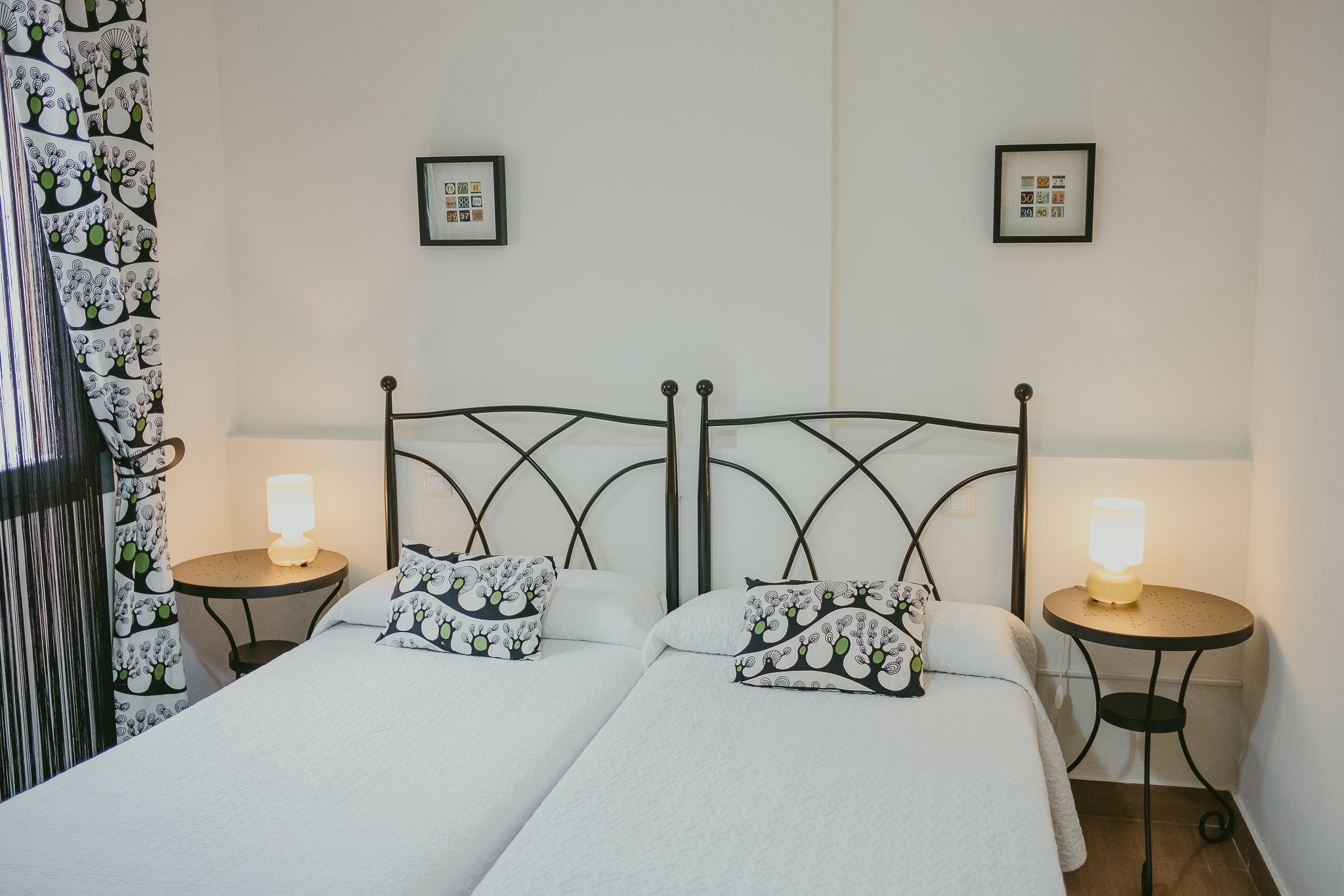 Una cama doble con dos almohadas, una mesita de noche con lámpara y una cortina con estampado floral.