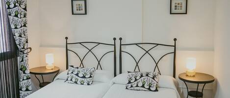 Una cama doble con dos almohadas, una mesita de noche con lámpara y una cortina con estampado floral.