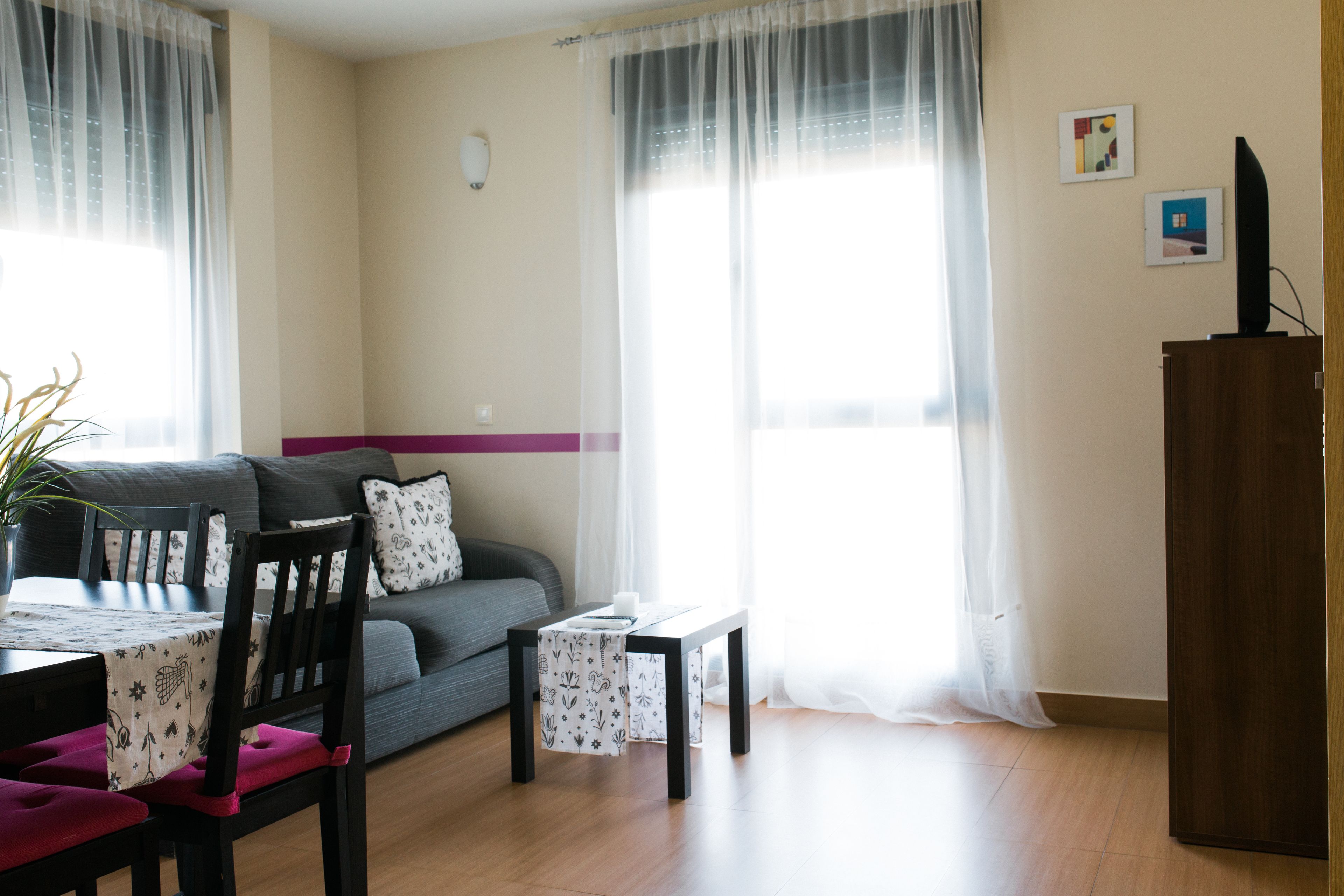Un salon avec un canapé, une table à manger avec des chaises, une petite table avec une bougie et un téléviseur posé sur un meuble.