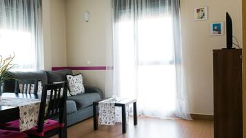Un salon avec un canapé, une table à manger avec des chaises, une petite table avec une bougie et un téléviseur posé sur un meuble.