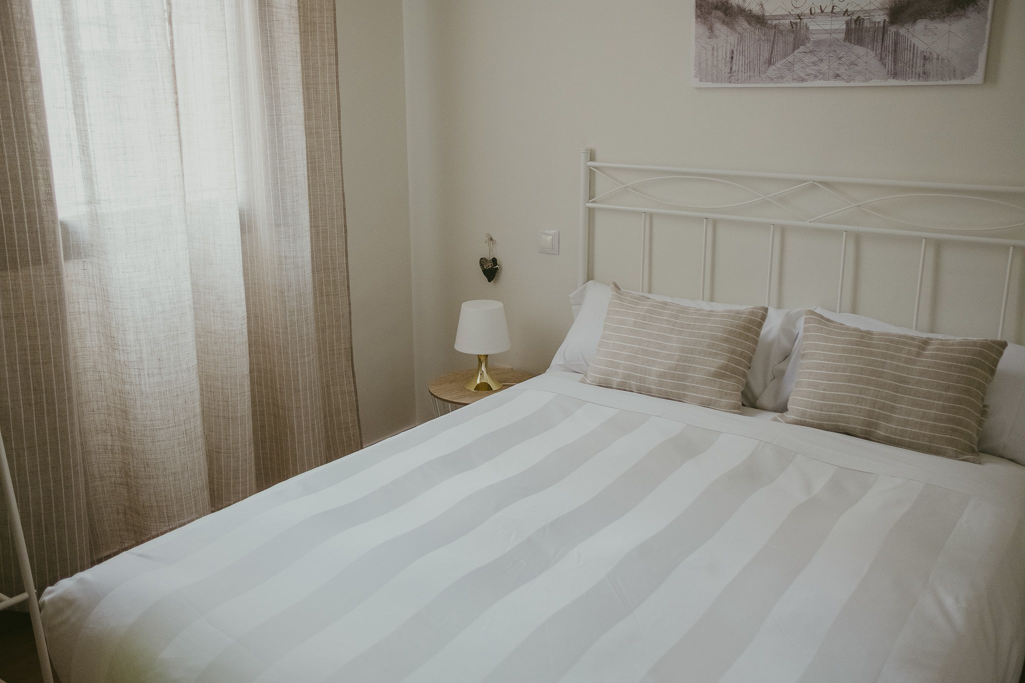 A neatly made bed with striped bedding, a bedside lamp, and a heart-shaped decoration on the wall.
