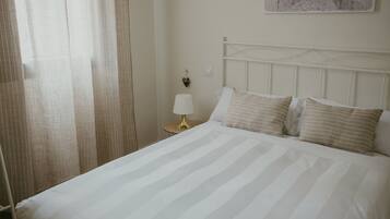 A neatly made bed with striped bedding, a bedside lamp, and a heart-shaped decoration on the wall.