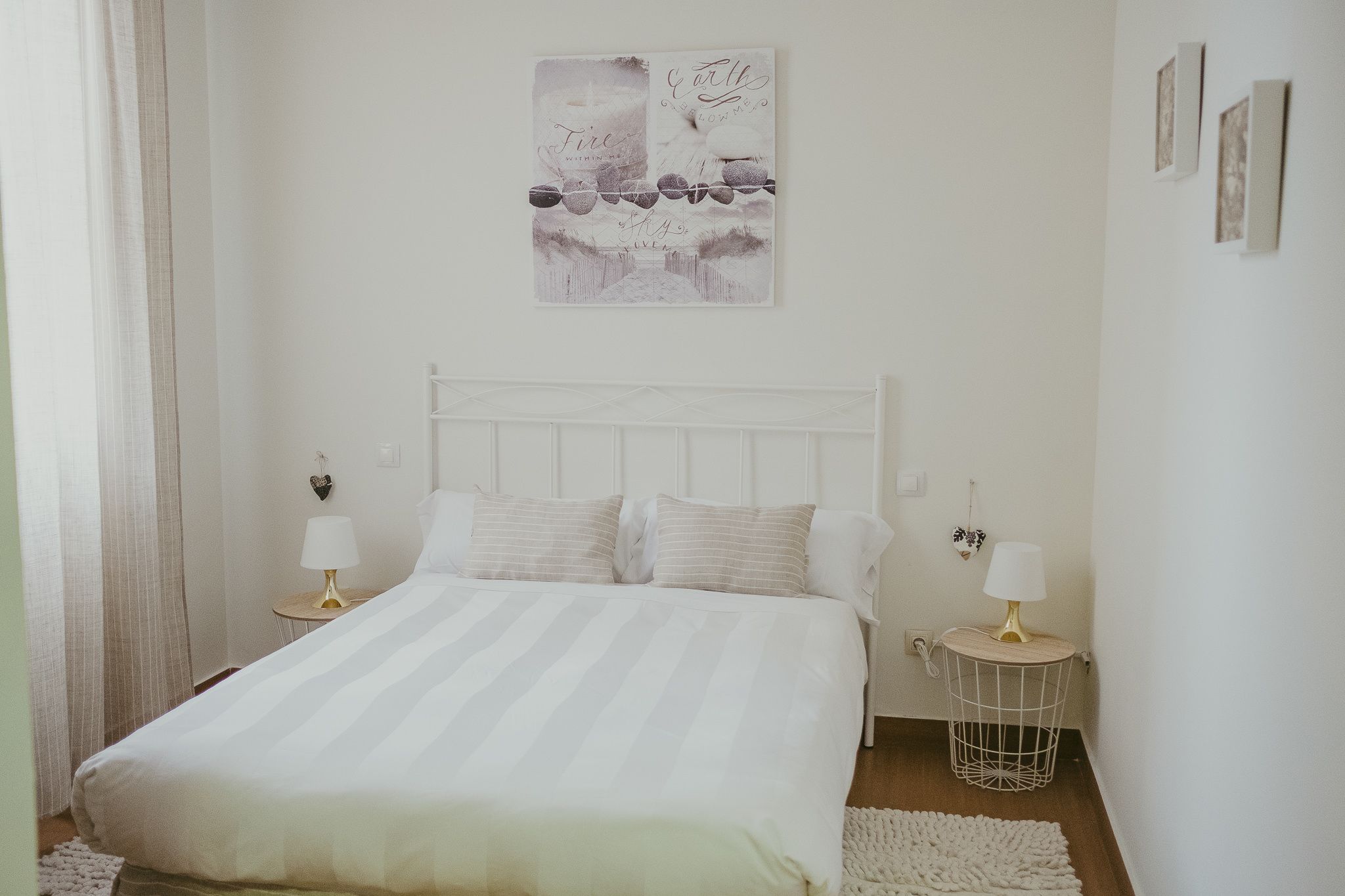 Un dormitorio con una cama blanca, dos mesitas de noche con lámparas, un cabecero blanco y una obra de arte colgada en la pared.