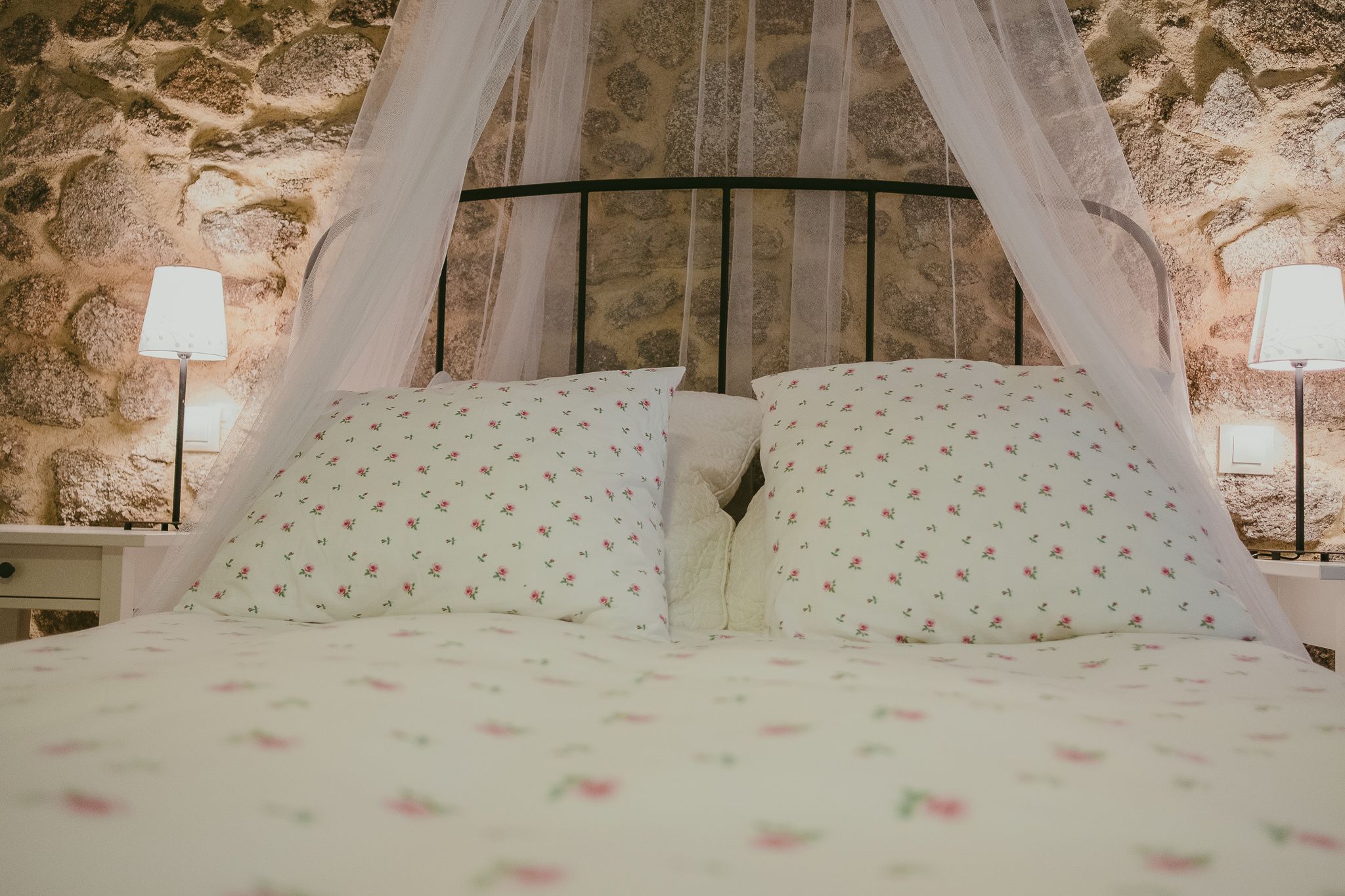 A bed with a canopy, floral bedding, and stone walls.