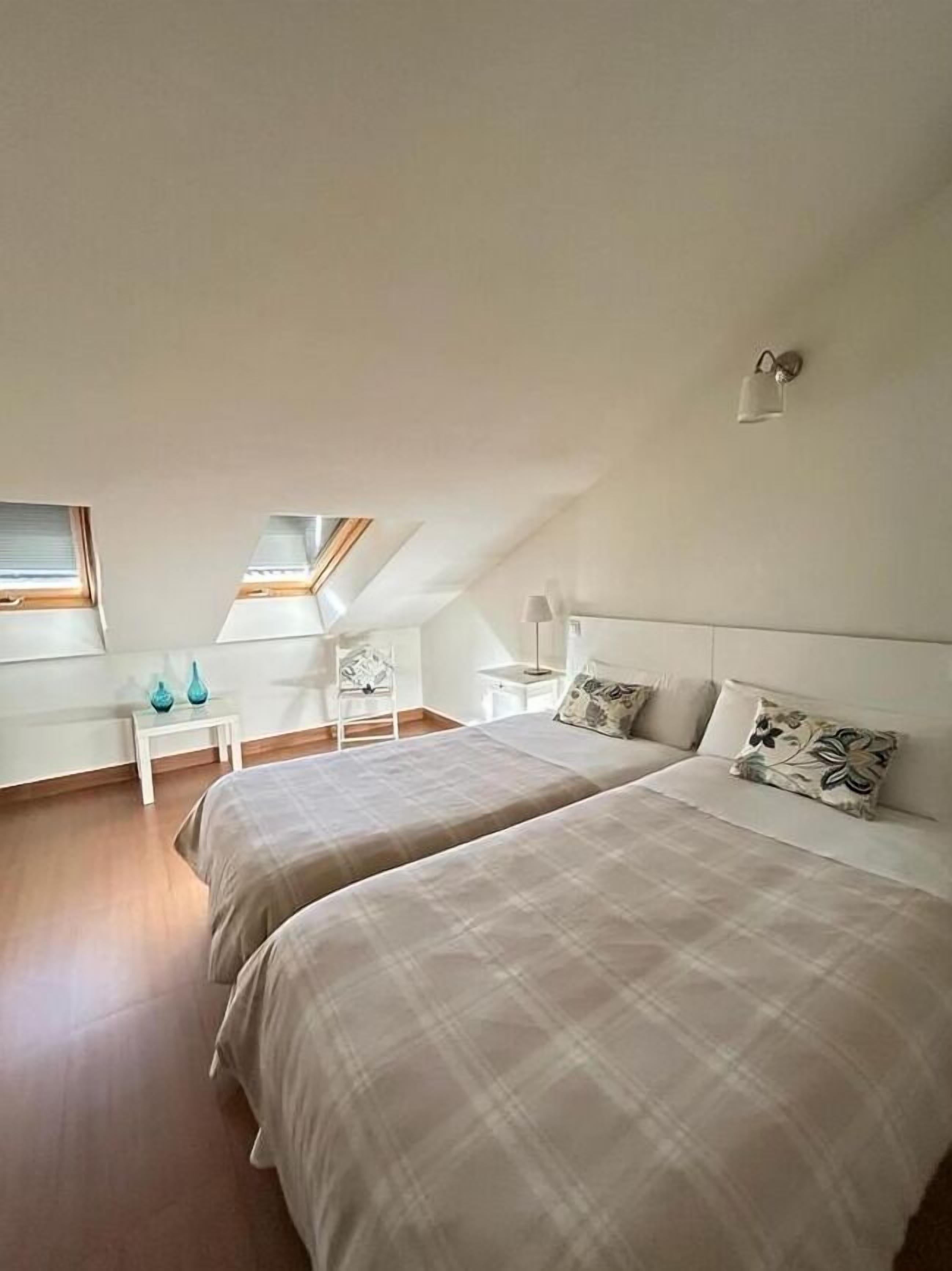 Ein Schlafzimmer mit zwei Betten, einem kleinen weißen Nachttisch, einem Stuhl und einem Oberlicht.