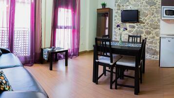 A compact living space with a sofa, dining table, chairs, a small kitchen area with a microwave, and a stone wall.