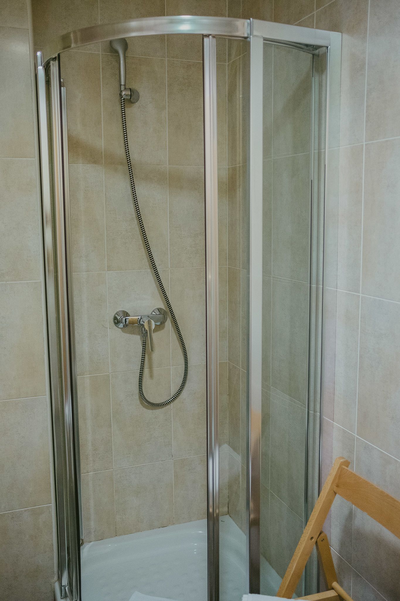 A glass-enclosed shower stall with a handheld showerhead and a wall-mounted faucet.