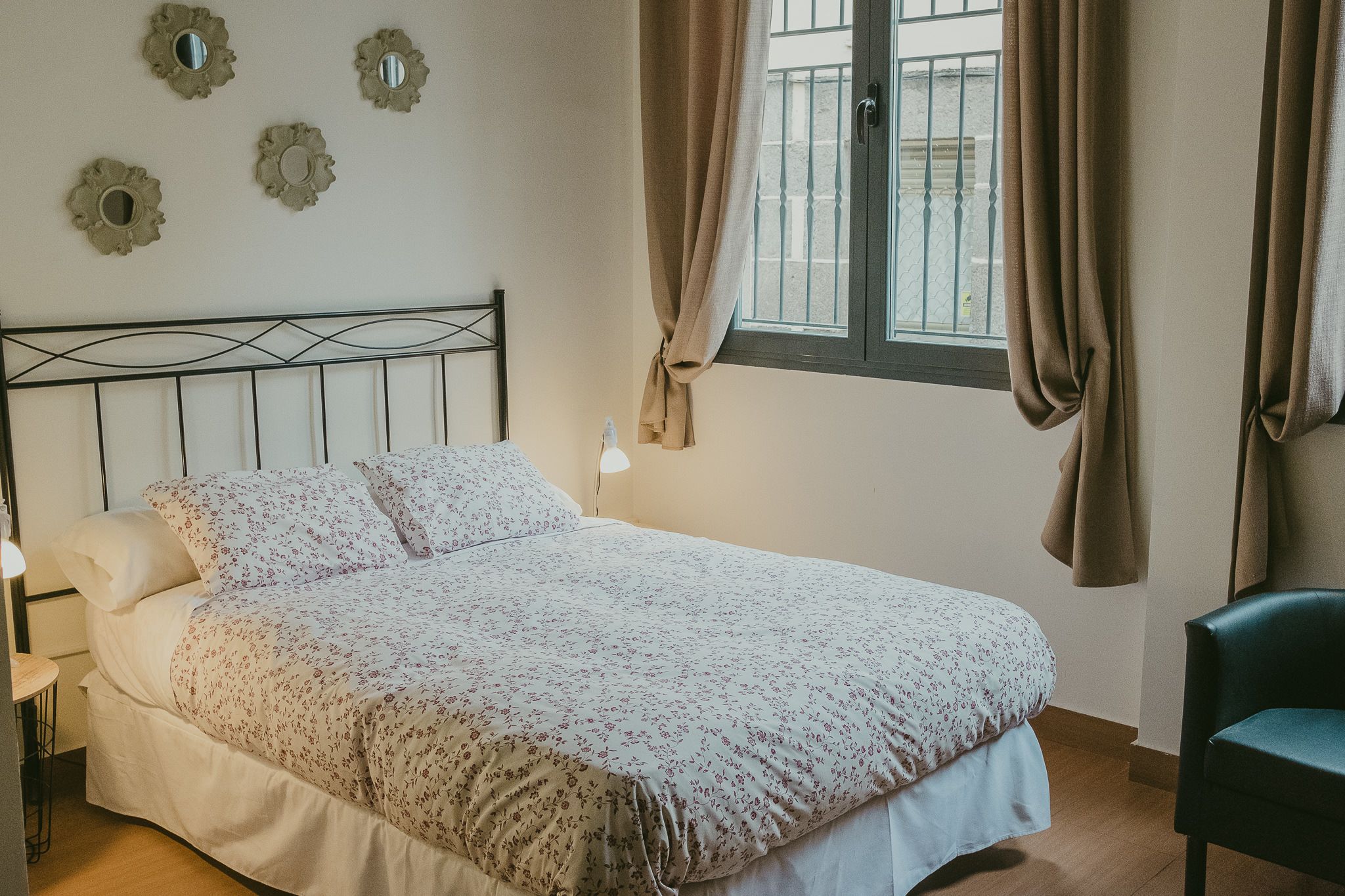 Una cama bien hecha con ropa de cama floral, una lámpara de noche y espejos decorativos en la pared.