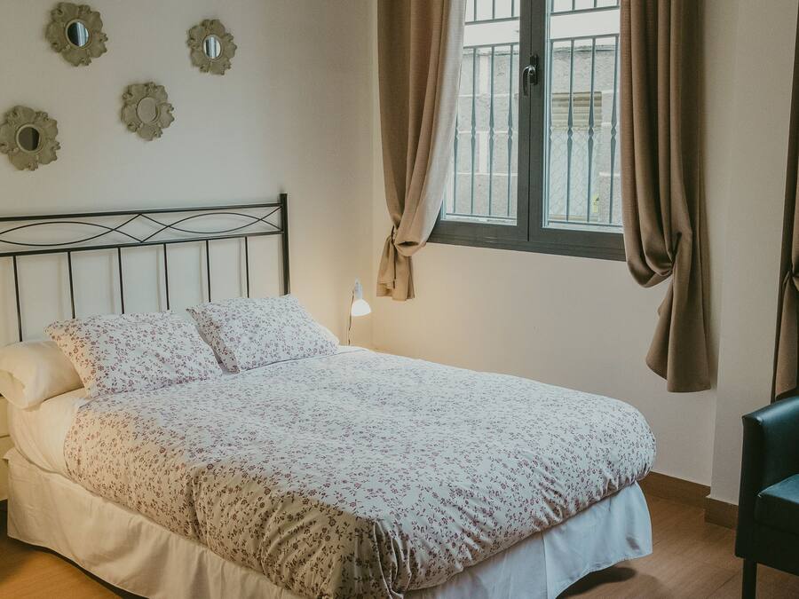 A neatly made bed with floral bedding, a bedside lamp, and decorative wall mirrors.