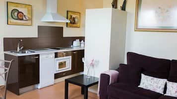 Una cocina compacta equipada con lavavajillas, horno y un comedor con mesa y sofá.