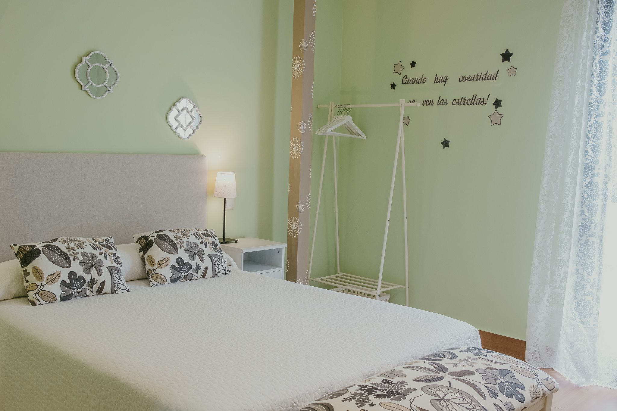 A neatly made bed with patterned pillows, a bedside table with a lamp, and a wall with decorative star and moon stickers.