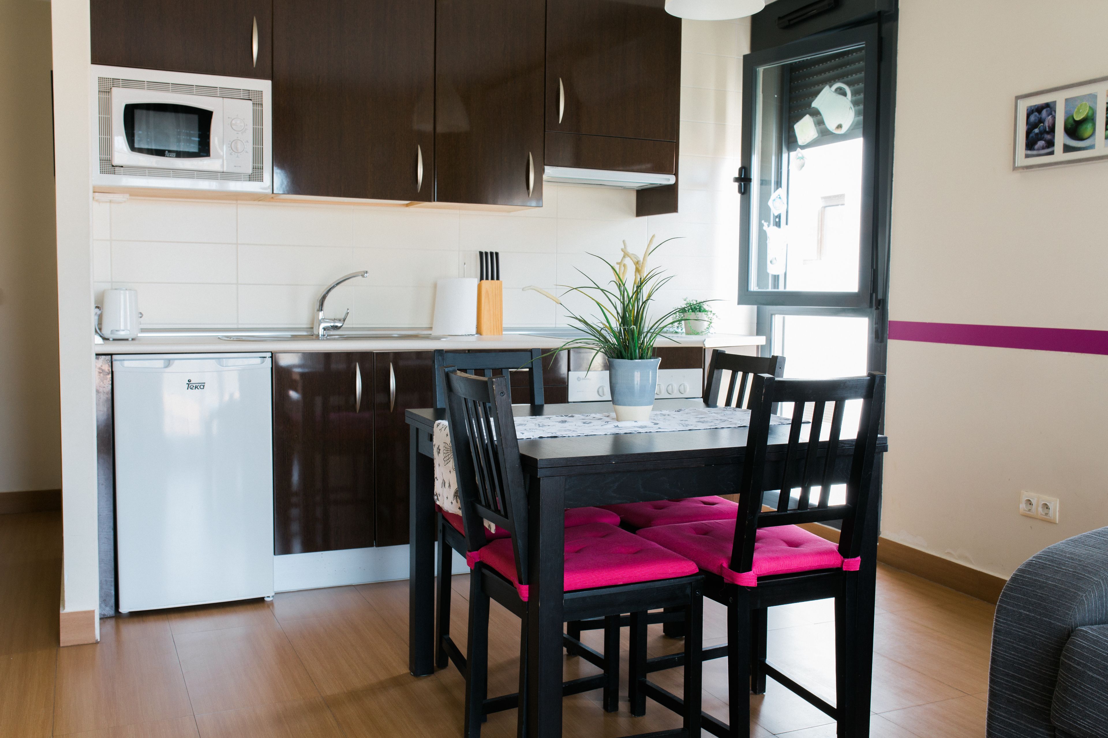 A compact kitchen with dark wooden cabinets, a microwave, a sink, and a dining area with two chairs and a table.