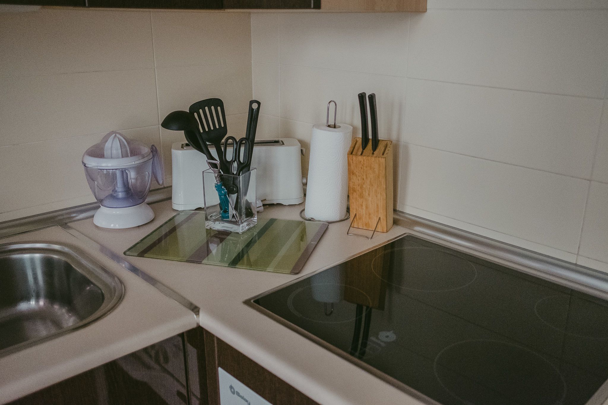 Een keuken met een spoelbak, een broodrooster, een papieren handdoekhouder en een messenblok.