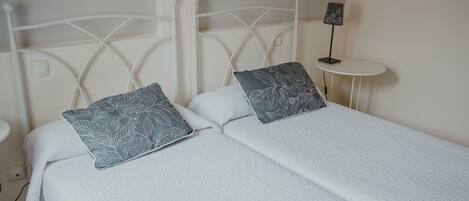 A double bed with white bedding and leaf-patterned pillows, a white metal headboard, and a small bedside table with a lamp.