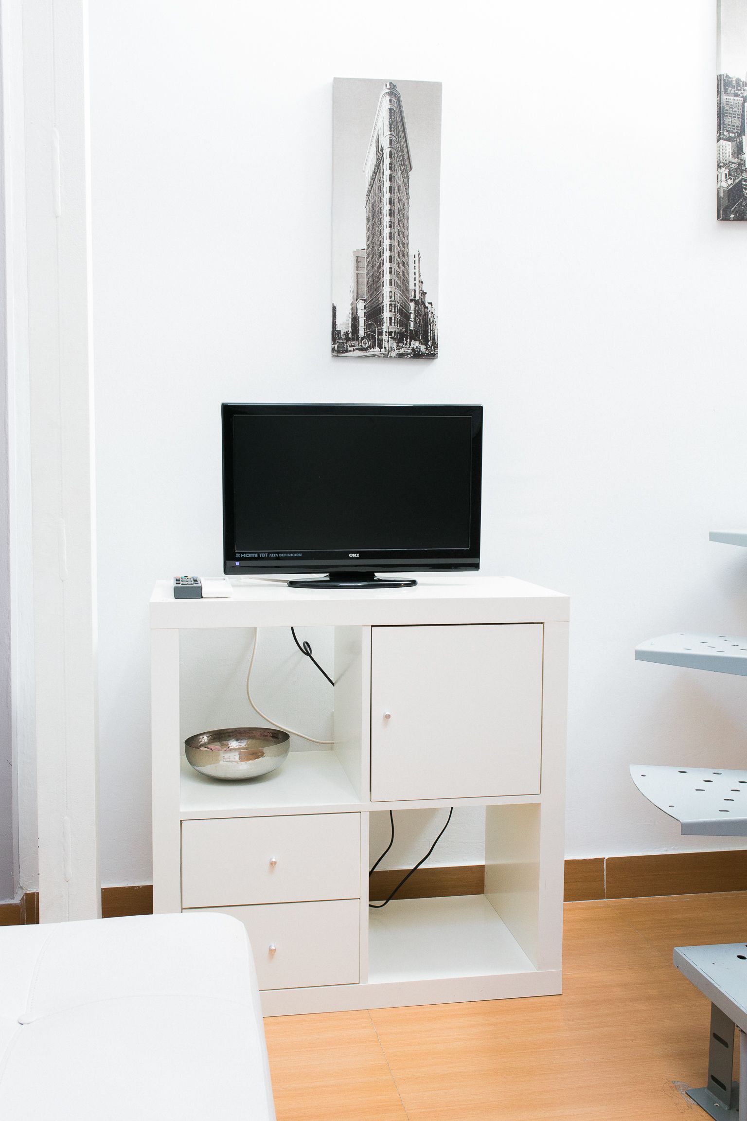 A white TV stand with a flat-screen TV, a small bowl, and a drawer.