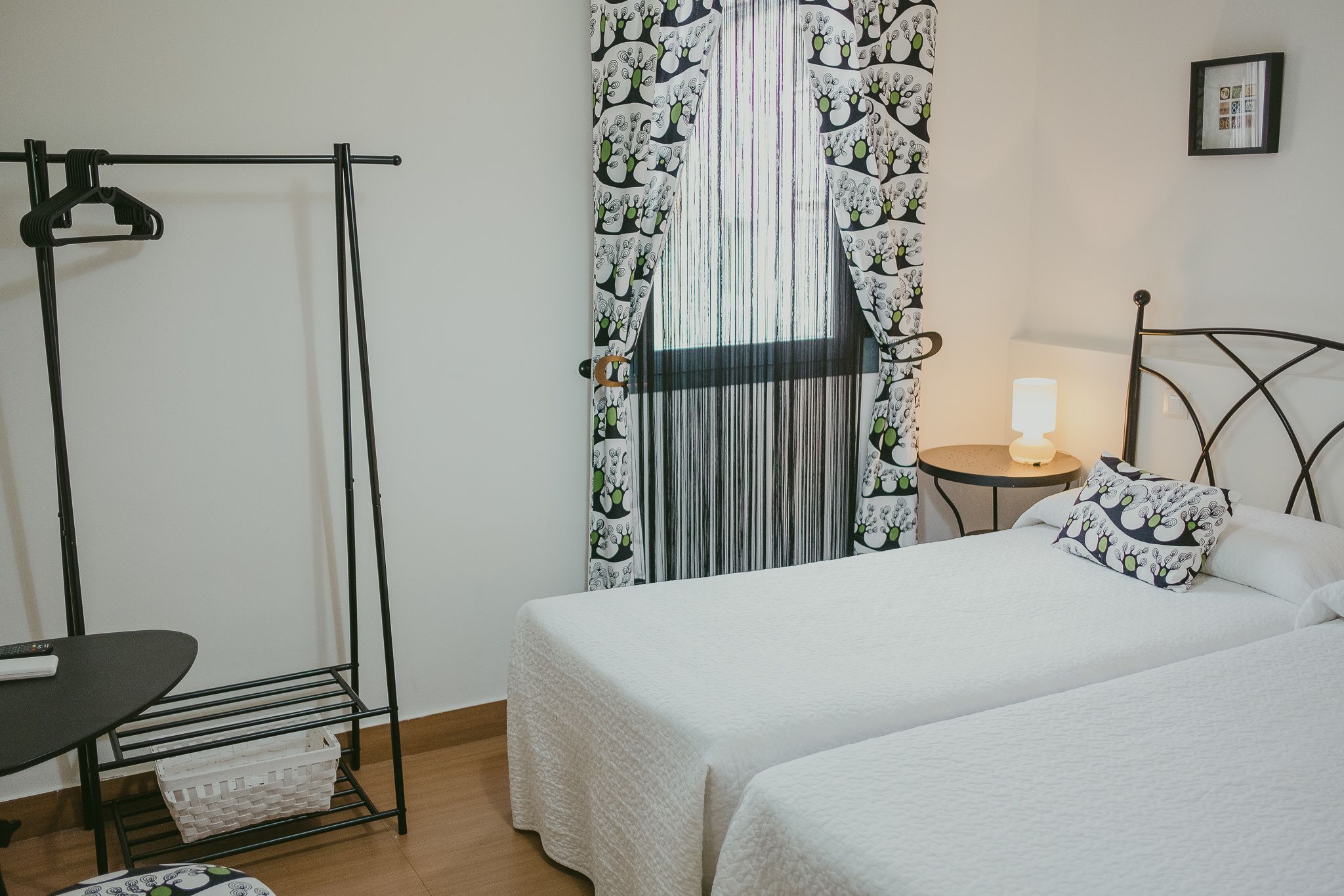 A bedroom with two beds, a wardrobe, a table with a lamp, and a curtain with a cactus pattern.