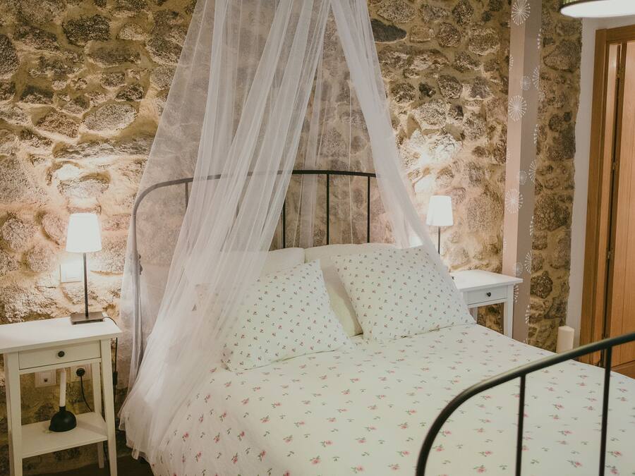 Un dormitorio con pared de piedra, cama con dosel, mesita de noche con lámpara y puerta de madera.