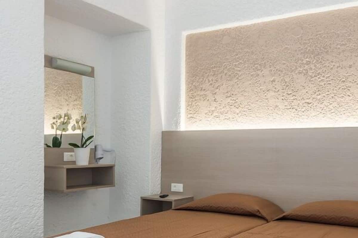 Habitación de hotel con dos camas, cada una con una colcha marrón acolchada y toallas blancas. Hay una mesita de noche con una lámpara y una planta pequeña.