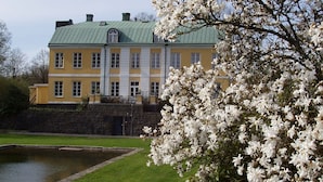 A large, yellow building with a green roof, surrounded by a well-maintained lawn and a small pond. - Wapnö Gårdshotell (Halmstad)