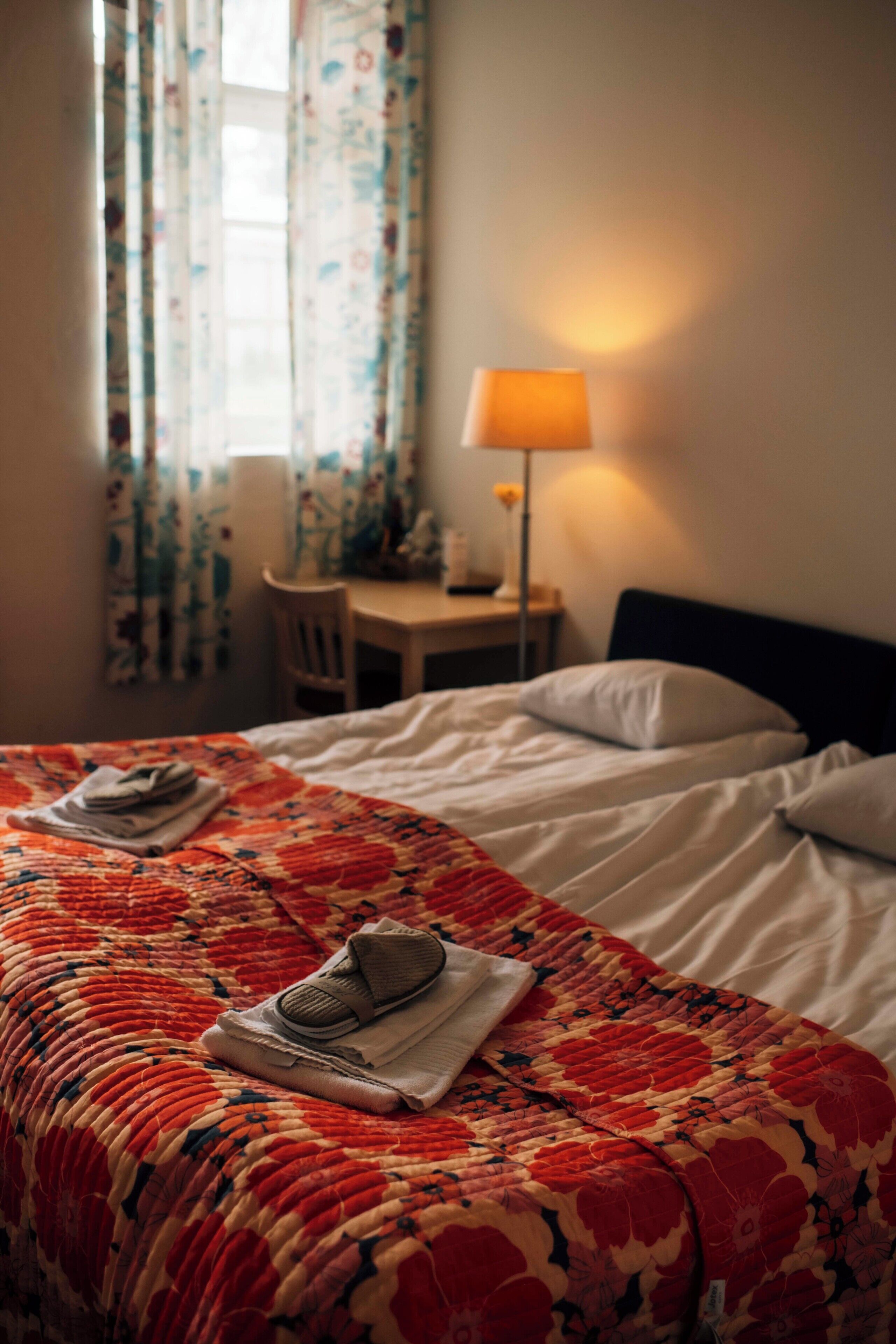 A hotel room with a bed, a chair, a desk, and a lamp.
