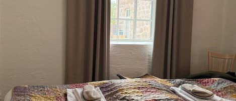 A bed with a colorful quilt, a wooden chair, and a window with curtains.