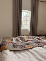 Una cama con un edredón colorido, una silla de madera y una ventana con cortinas.