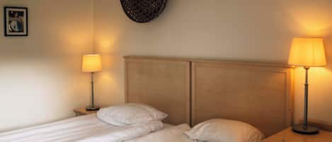 A double bed with two bedside tables, each with a lamp, in a room with a plain wall and a framed picture.