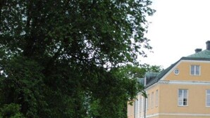 A building with a traditional architectural style, a paved pathway, and lush greenery. - Wapnö Gårdshotell (Halmstad)
