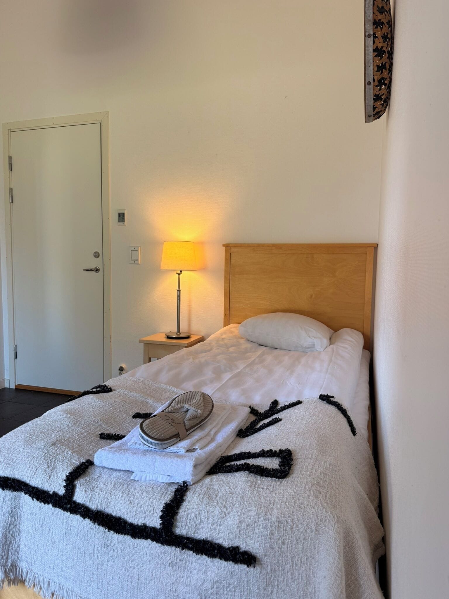 Une chambre d’hôtel avec un lit, une table de chevet avec une lampe, une porte et un mur orné d’un motif décoratif.