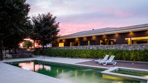 Una piscina con sillas de descanso, un muro de piedra y un edificio con ventanas y luces.