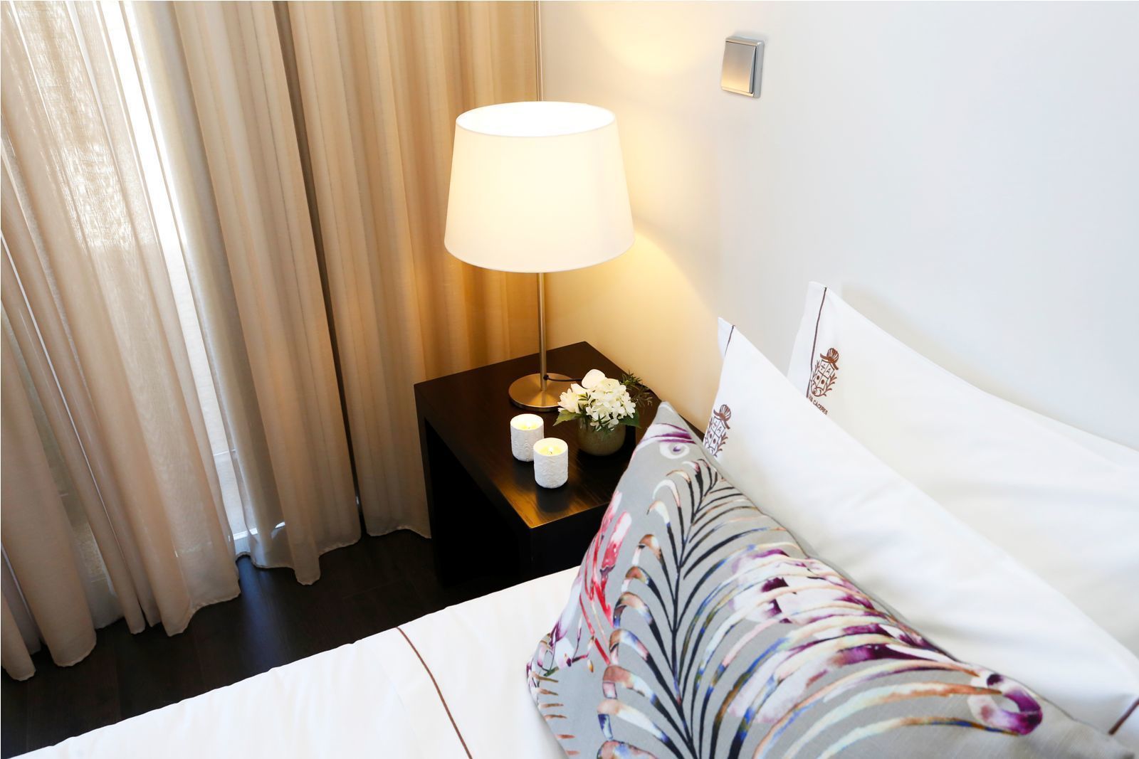 A hotel room with a bed, a nightstand with a lamp, and a vase with flowers.