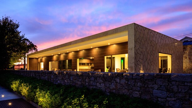 Un edificio moderno con fachada de piedra, ventanas grandes y un muro de piedra al frente.