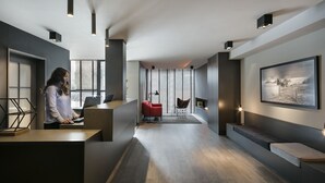 A modern office space with a long reception desk, a red chair, a bench, and a large framed picture on the wall. - Hotel Upper Diagonal (Barcelona)