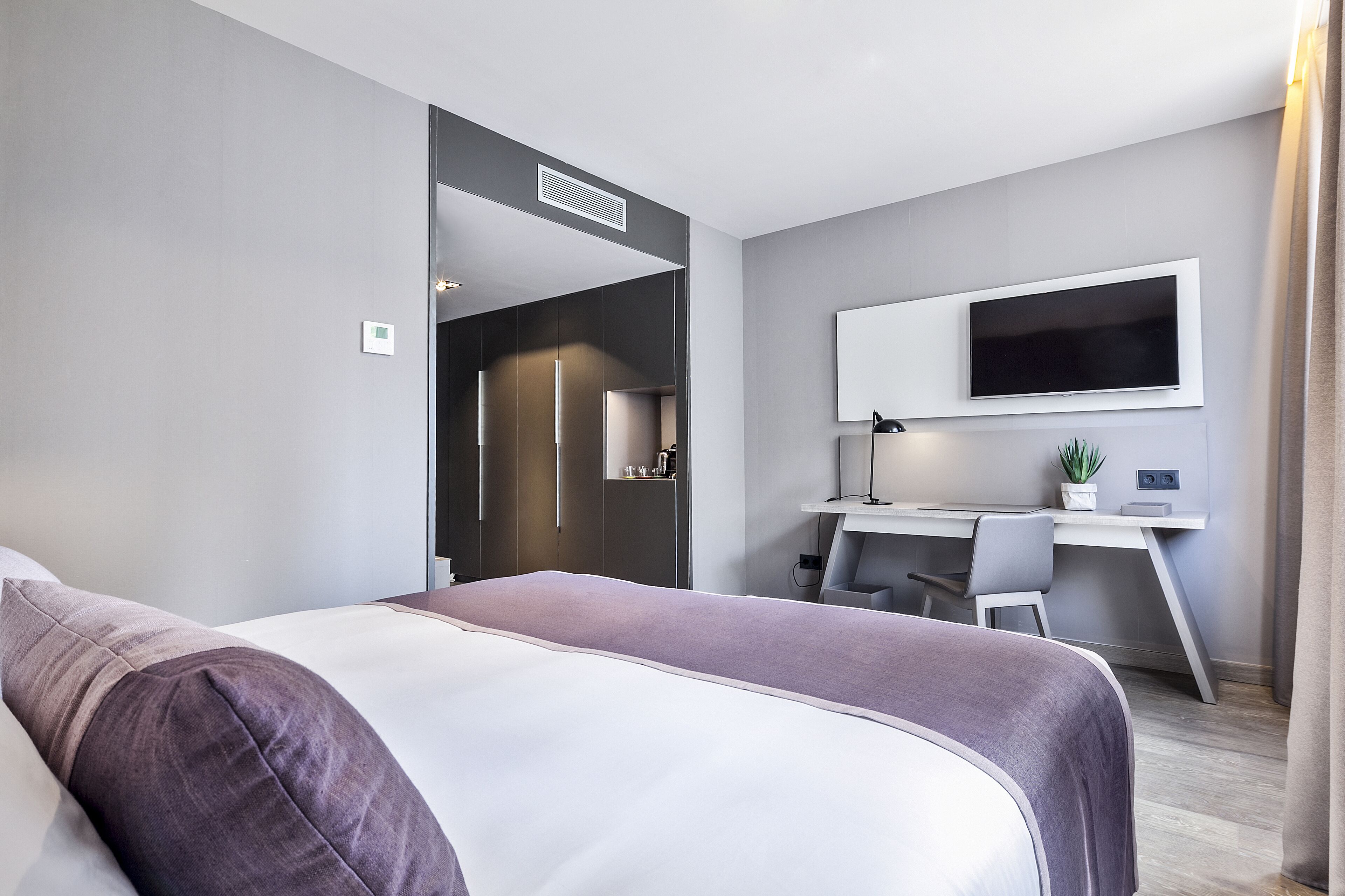 A modern hotel room with a bed, a desk, and a TV.
