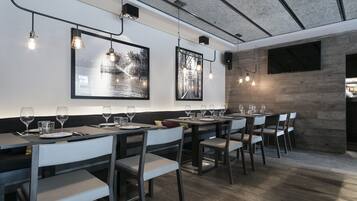 Uma sala de jantar moderna com mesas de madeira, cadeiras brancas e iluminação pendente.