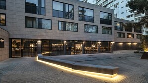 A modern building with multiple floors, large windows, and a well-lit outdoor area with a bench.