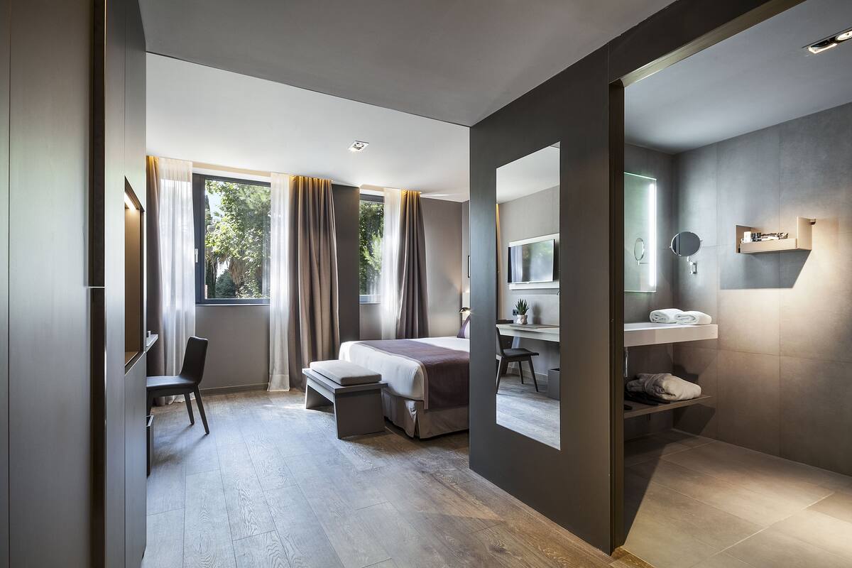 A modern hotel room with a bed, desk, chair, and a large mirror.