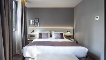 A modern hotel room with a large bed, bedside tables, a nightstand, and a window with curtains.