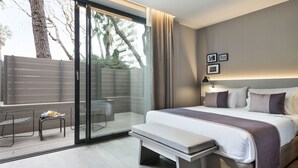 A modern hotel room with a large bed, a bench, a small table with a tray of breakfast, a sliding glass door to a balcony, and a city view.