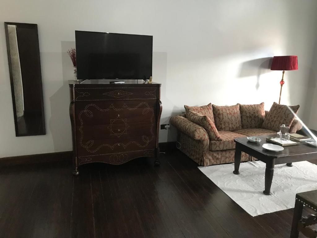A living room with a dark wooden cabinet, a flat-screen TV, a patterned sofa, a coffee table with a red lamp, and a white rug.