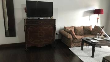 A living room with a dark wooden cabinet, a flat-screen TV, a patterned sofa, a coffee table with a red lamp, and a white rug.