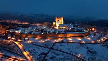 Un pueblo histórico amurallado con una destacada torre de iglesia, rodeado de edificios nevados y senderos iluminados.