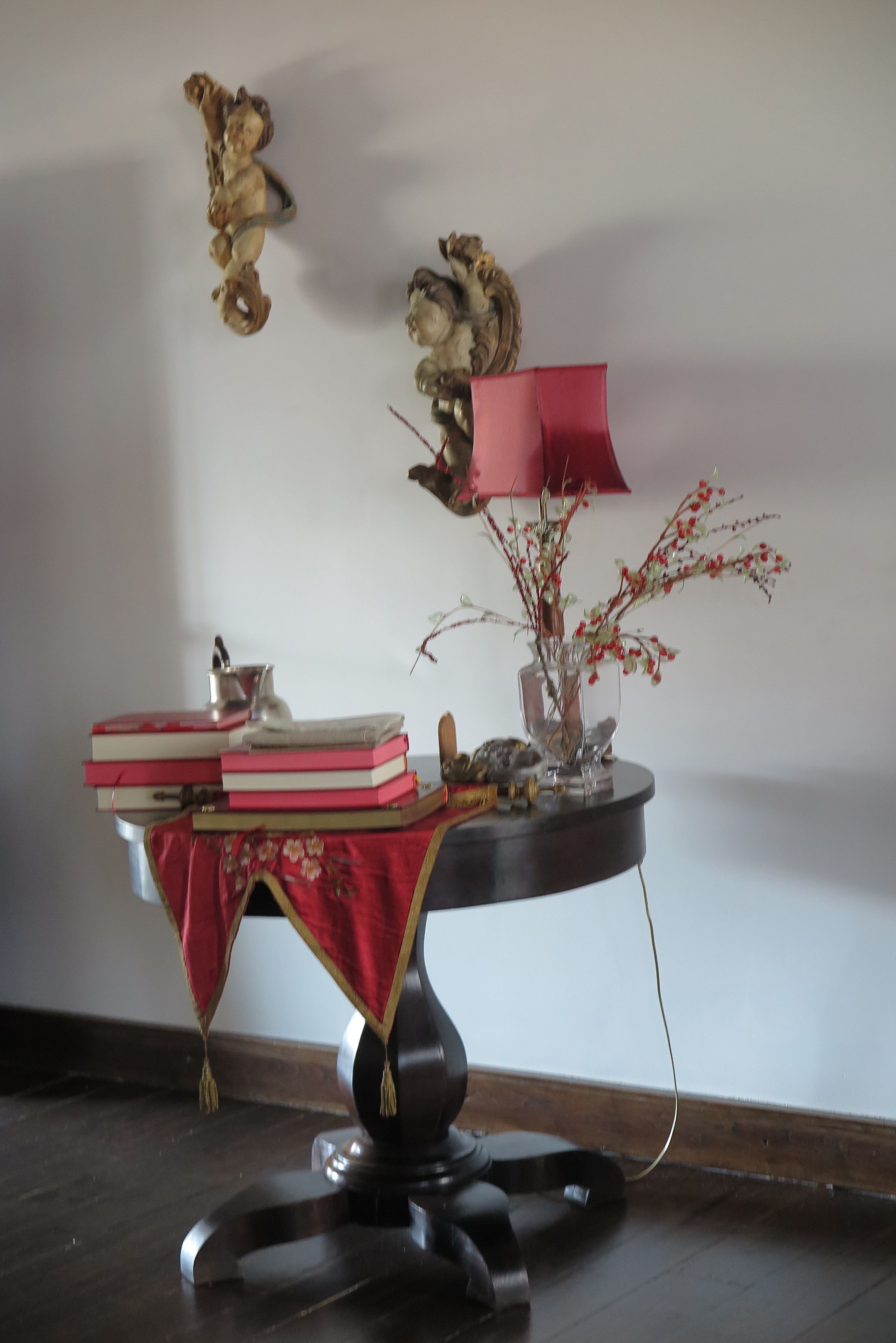 A table with books, a vase with branches, and a lamp.