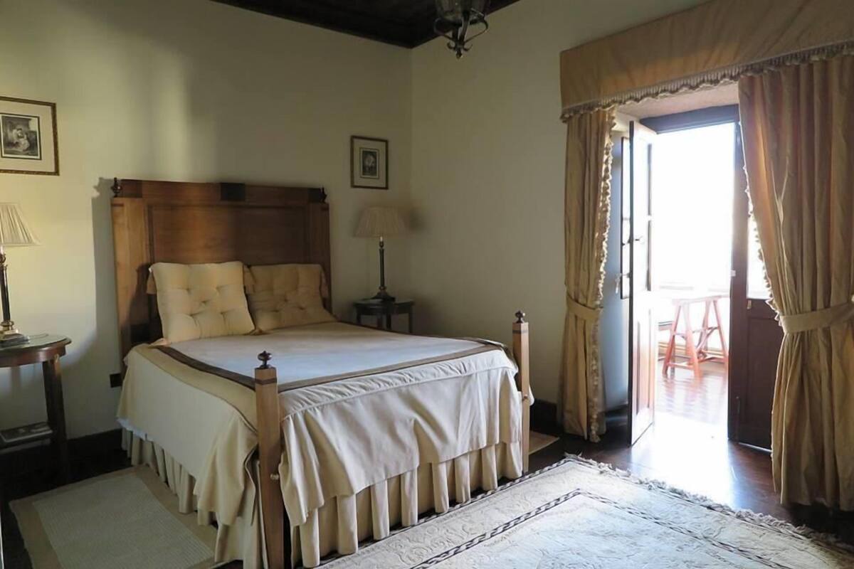 A bedroom with a wooden bed, a nightstand, a lamp, and a view of the outside.