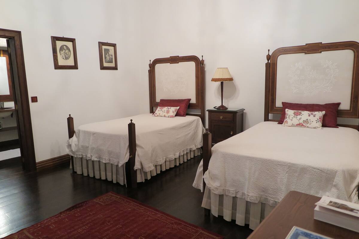 A room with two single beds, a nightstand with a lamp, and a small table with a book.