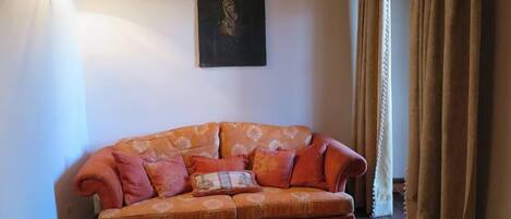 A living room with a patterned sofa, a wall-mounted painting, and a window with curtains.