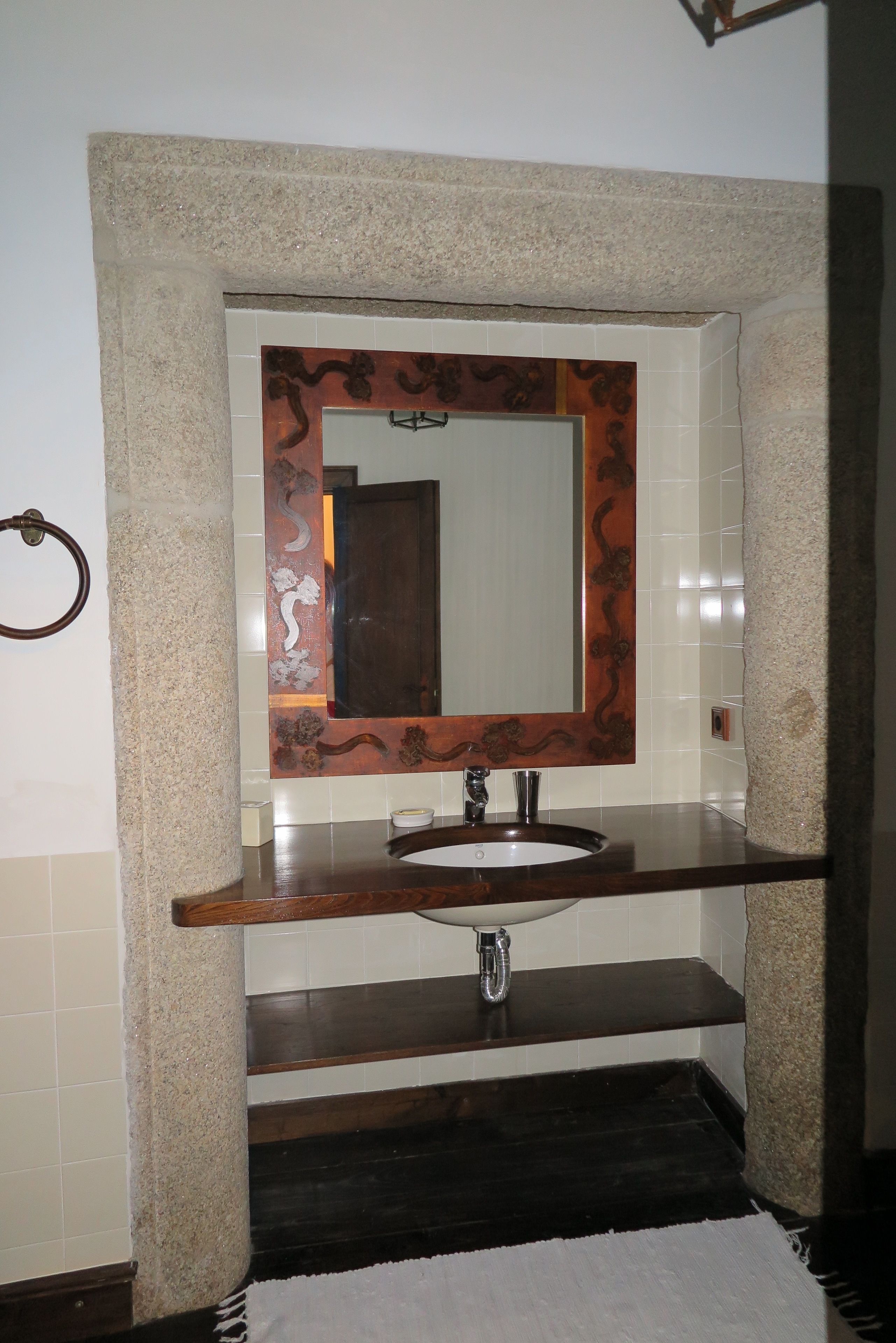A bathroom with a stone sink, a mirror with a decorative frame, and a towel ring.