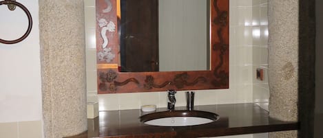 A bathroom with a stone sink, a mirror with a decorative frame, and a towel ring.