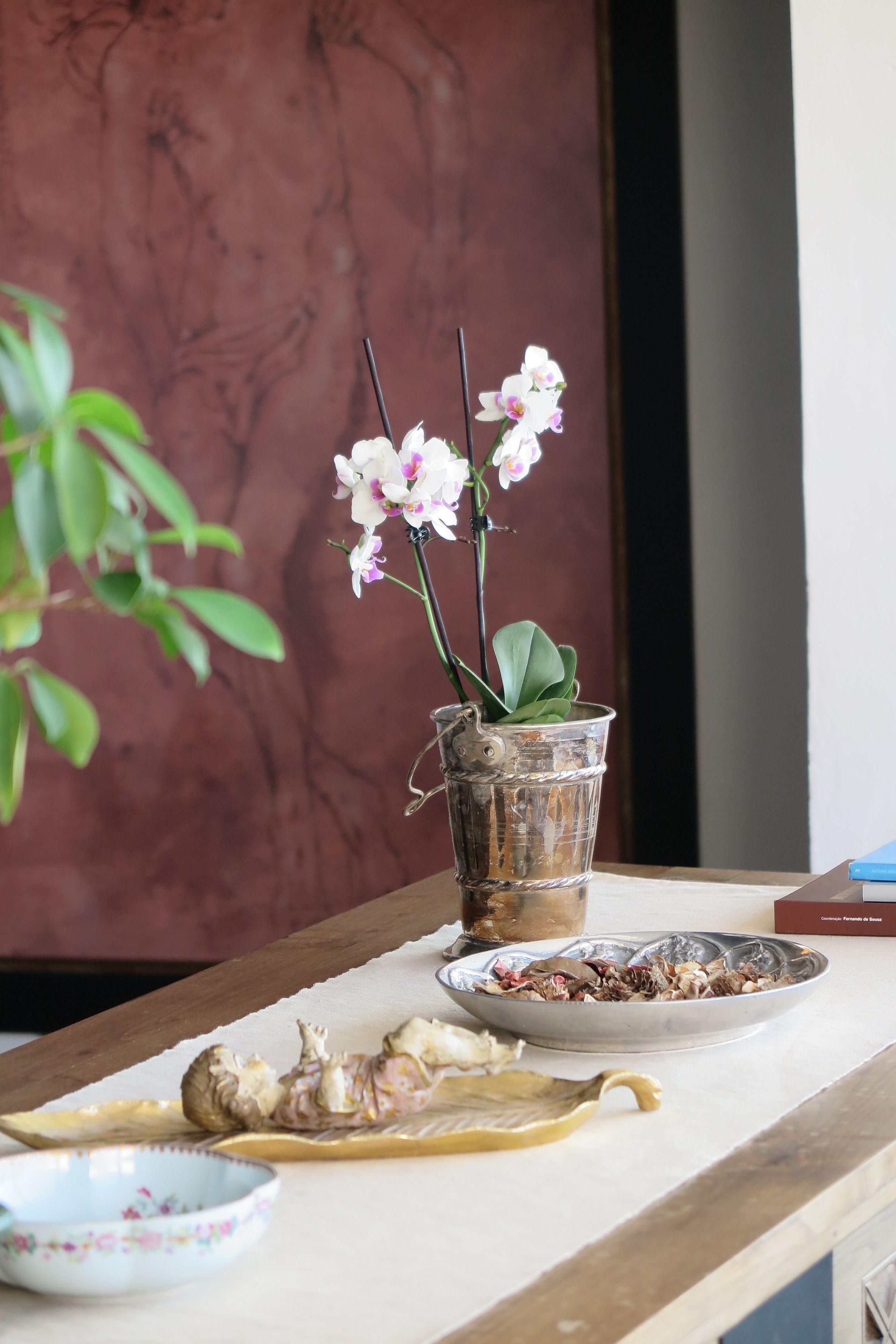 Une table ornée d’une orchidée en pot, d’un bol en métal et d’une assiette décorative.