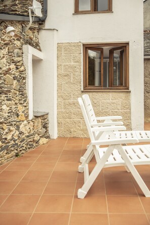A patio area with stone walls, a window, and white lounge chairs.
